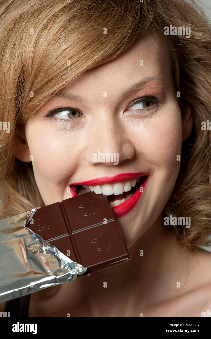 Happy woman biting into bar of dark chocolate Stock Photo