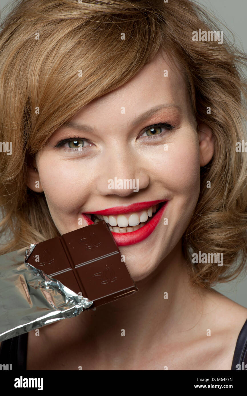 Happy woman biting into bar of dark chocolate Stock Photo