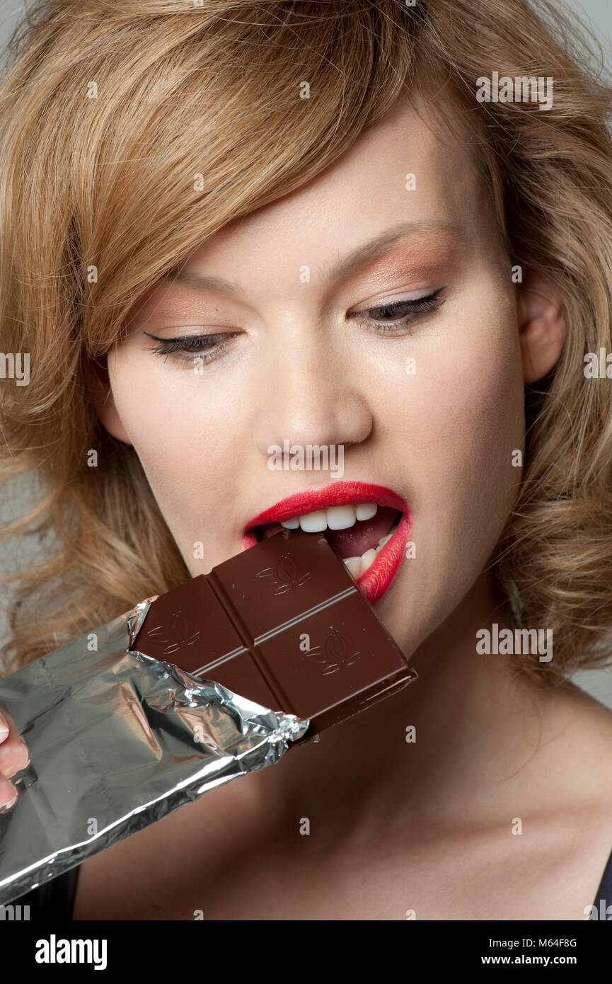 Woman biting into bar of dark chocolate Stock Photo