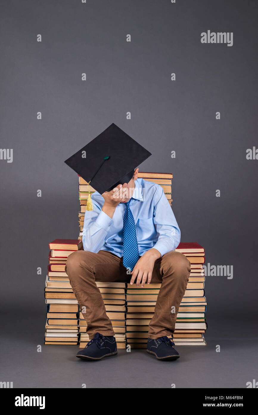 The boy is a professor, tired of studying, sitting on a throne from books, education funny idea Stock Photo