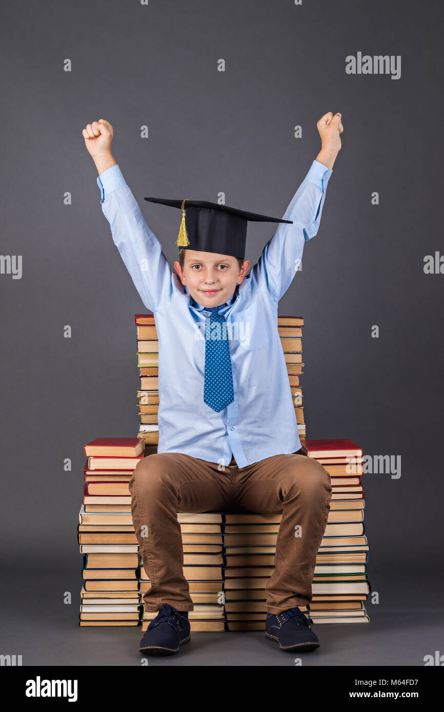 Education concept. Happy boy in mortarboard sitting on a throne from books Stock Photo