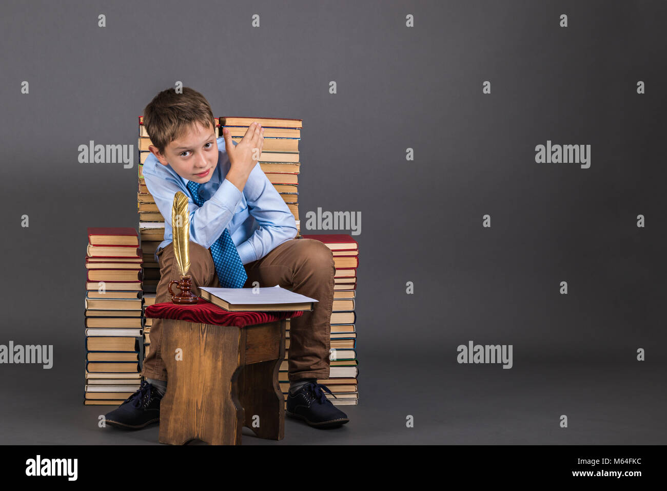 A boy with gold quill pen sitting in a throne of books and pointing his hand somewhere behind him Stock Photo