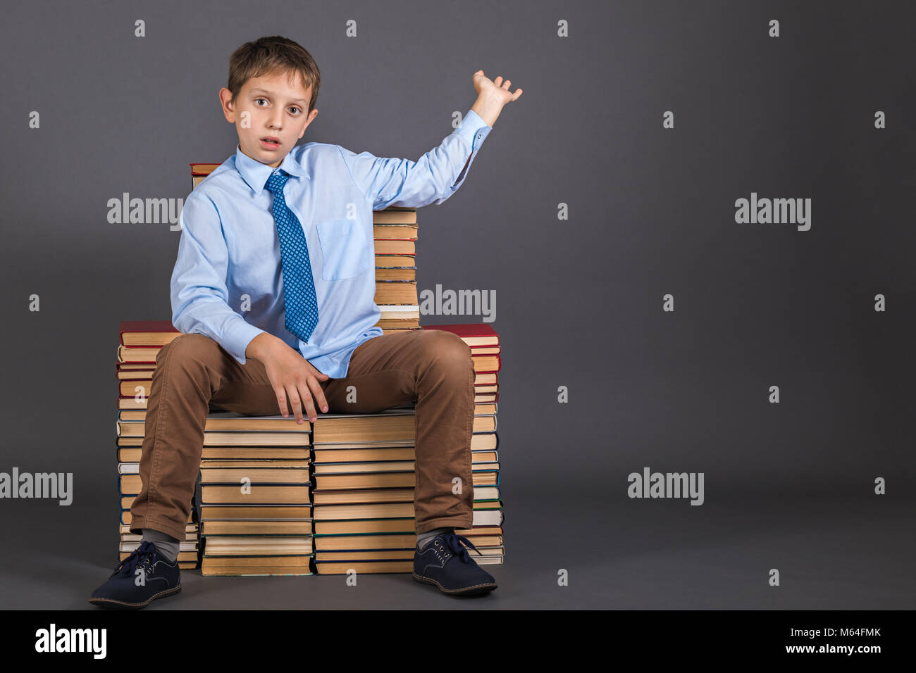 Education сoncept. Boy sitting on a throne from books, demonstrates something behind himself. Copy space for the demonstration object Stock Photo