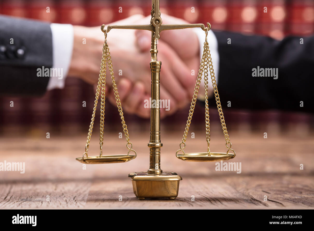Close-up Of Justice Scale On Wooden Desk In Front Of Businesspeople Shaking Hands Stock Photo