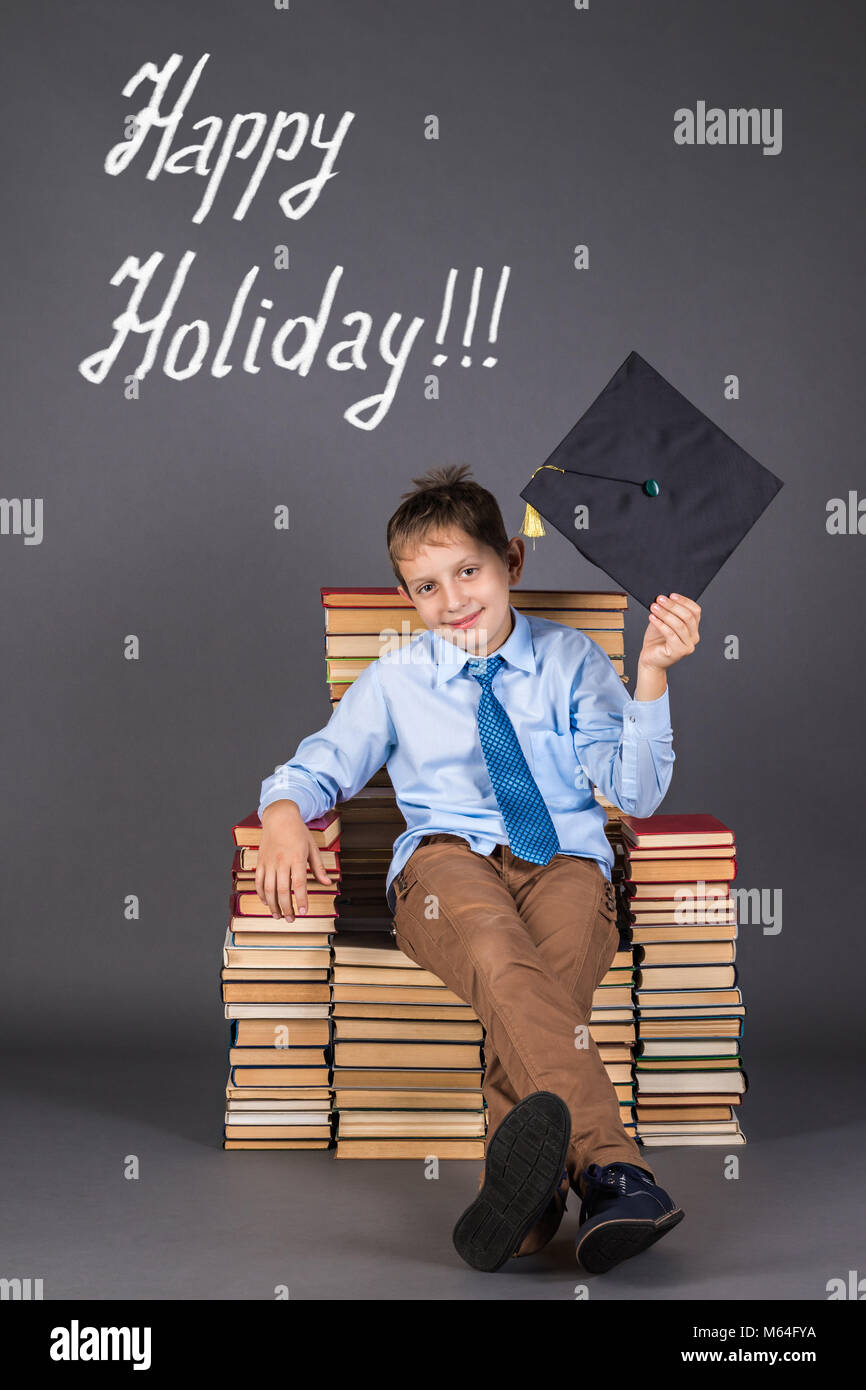 Education concept. The boy is leader, sitting in the throne from books, greets the audience with mortarboard Stock Photo