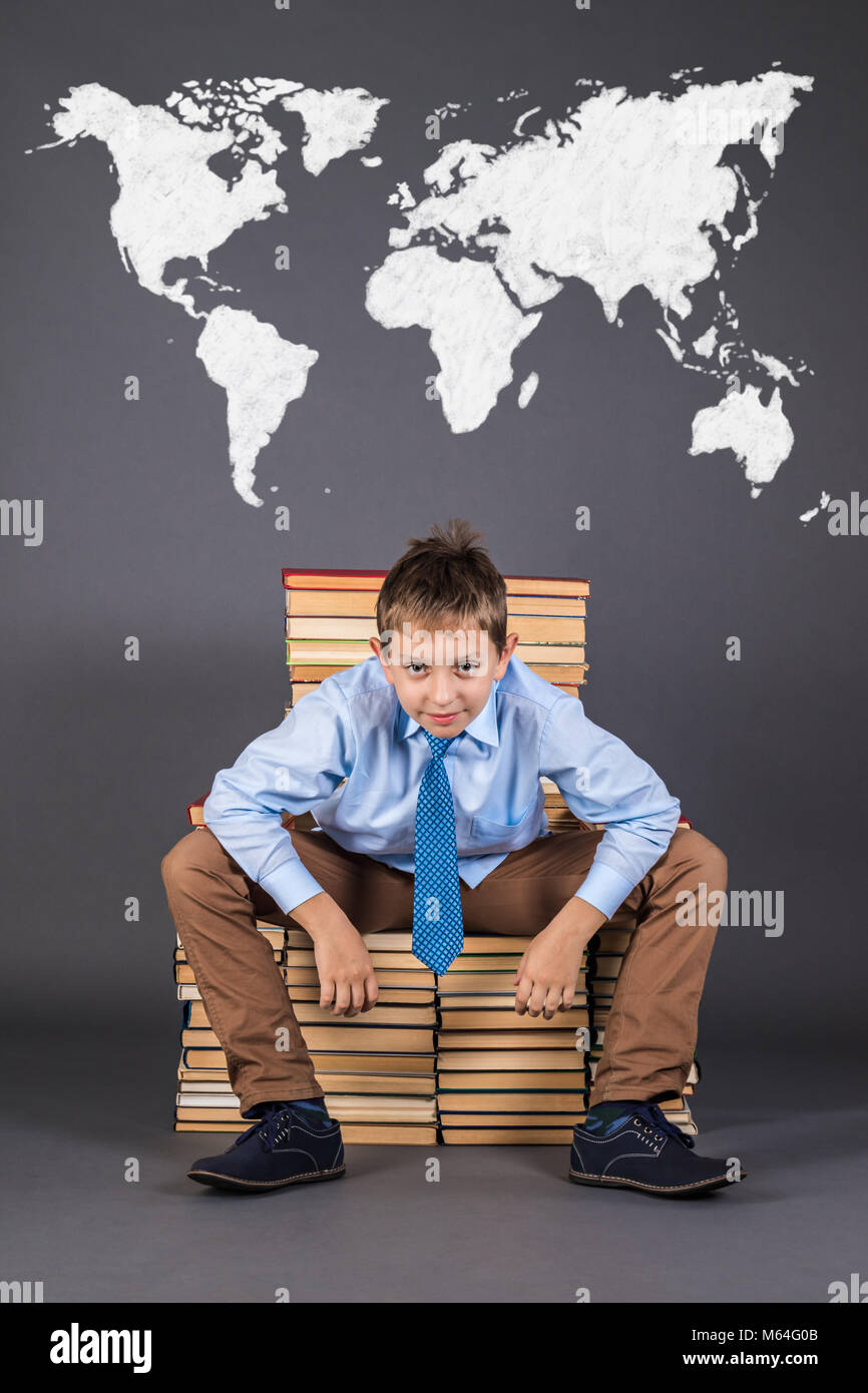 Education concept. The world map behind a cheerful boy sitting on a throne of books Stock Photo