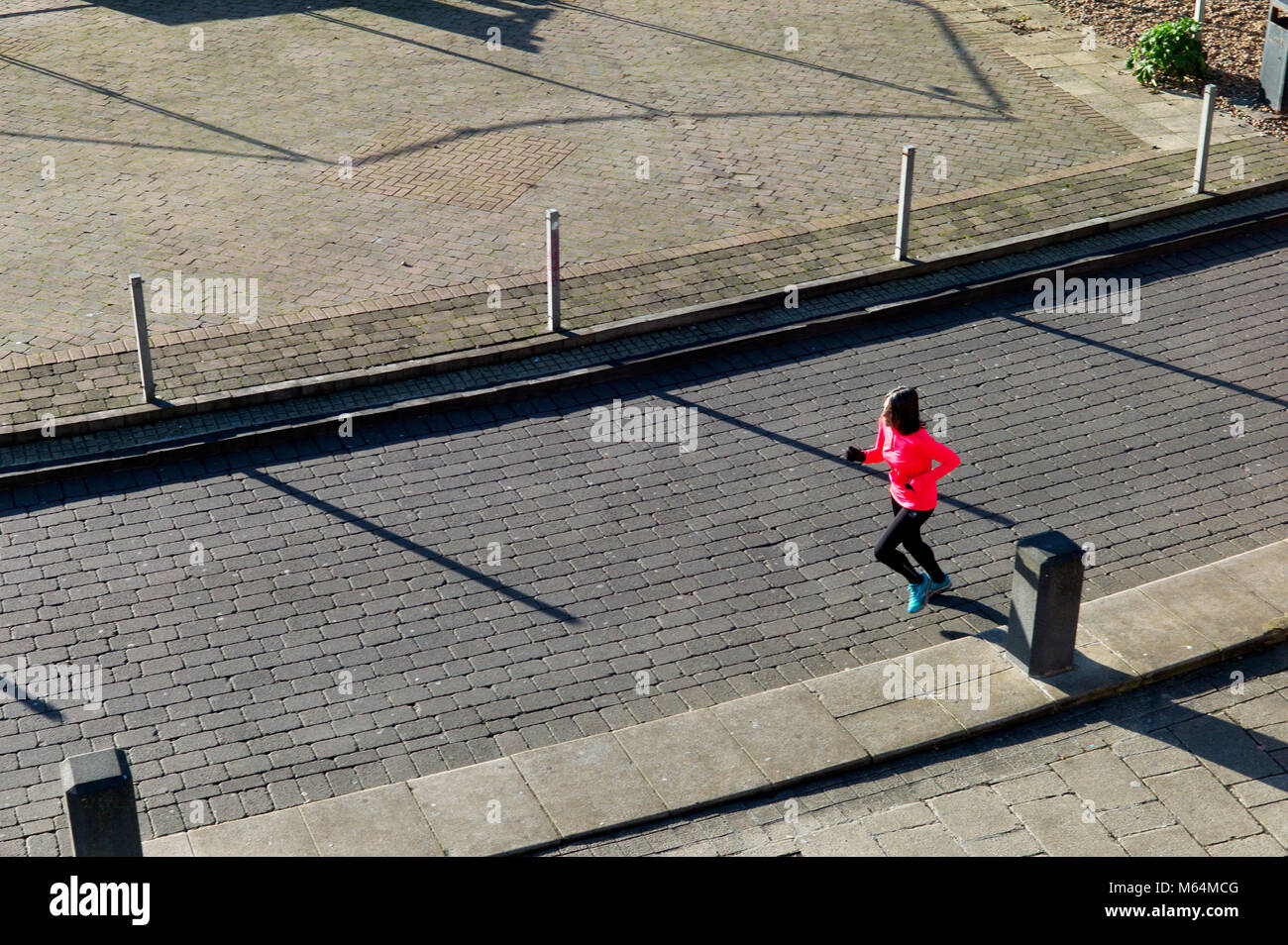 Solitary jogger in vivid pink top, seen from above, long shadows Stock Photo