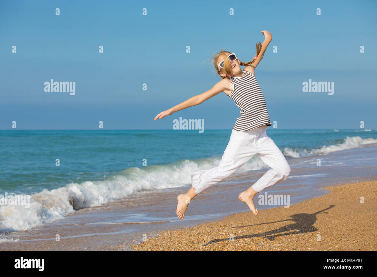 One happy little girl playing on the beach at the day time. She are dressed in sailor's vest. Kid having fun outdoors. Concept of sailor on vacation. Stock Photo