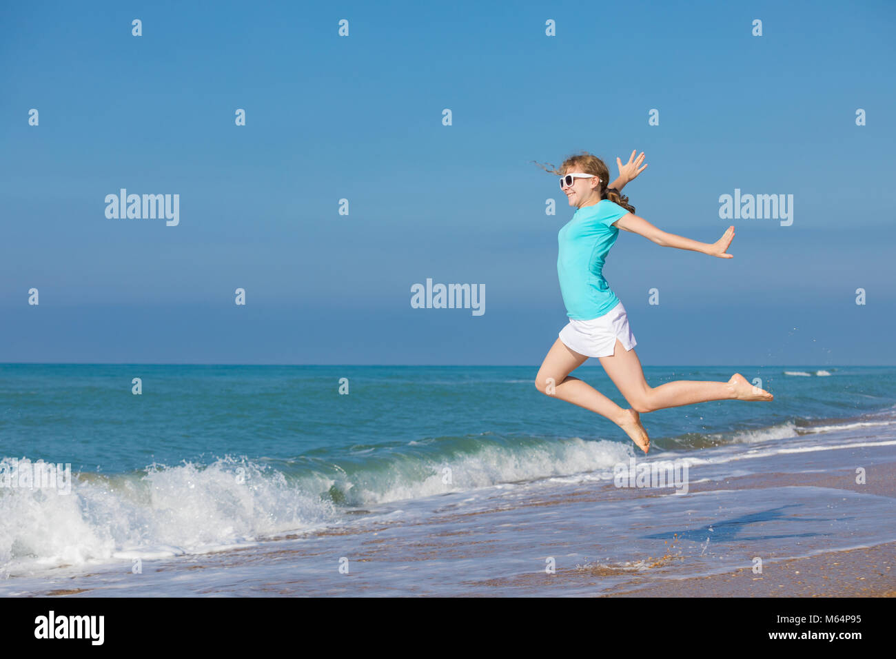 One teen girl jumping on the beach at blue sea shore in summer vacation at the day time. Kid having fun outdoors. Concept of happiness. Stock Photo