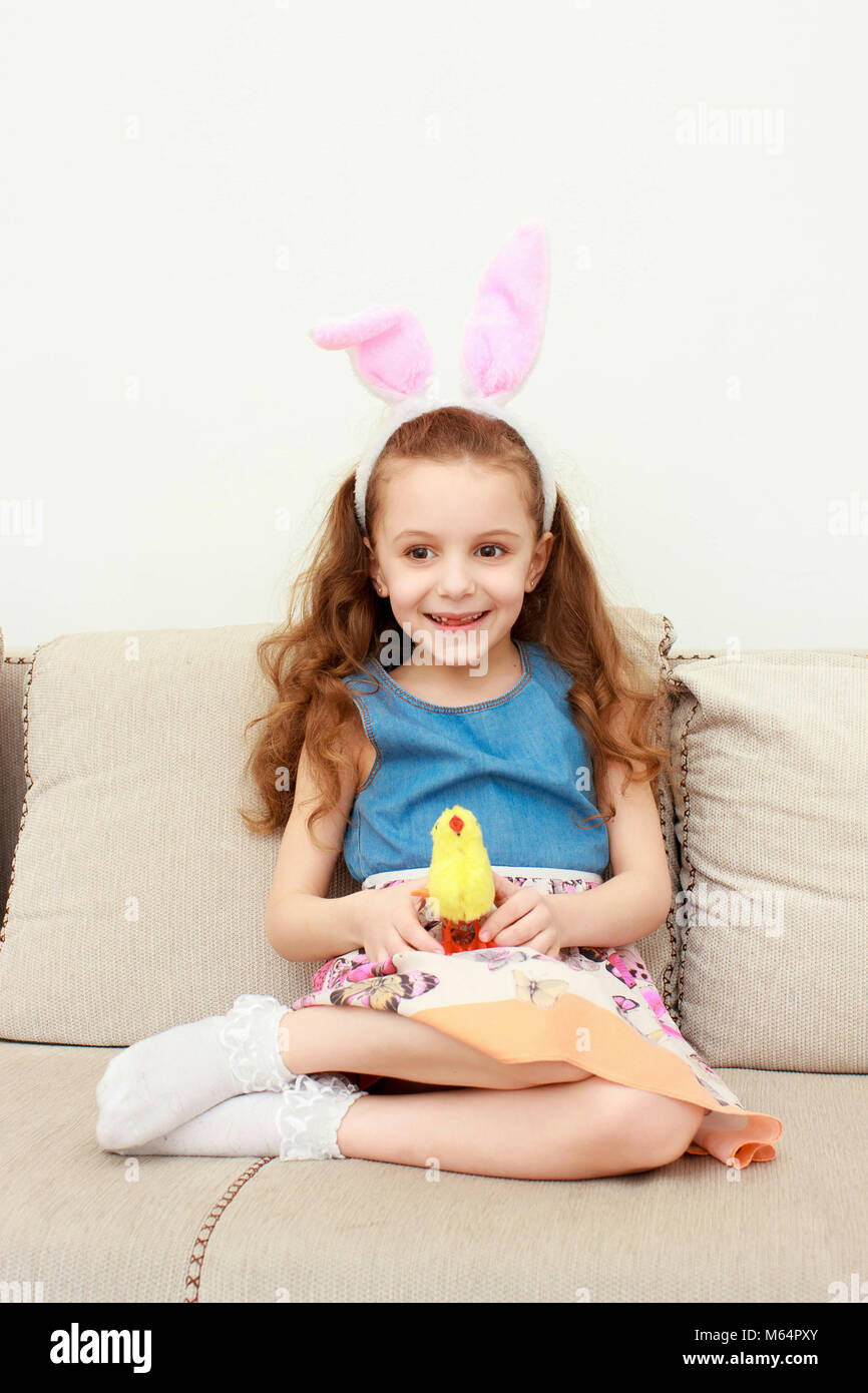 Portrait of little girl in easter pink bunny ears holding toy chick. Little girk in easter bunny ears at holiday. Cute little girl with bunny ears and Stock Photo