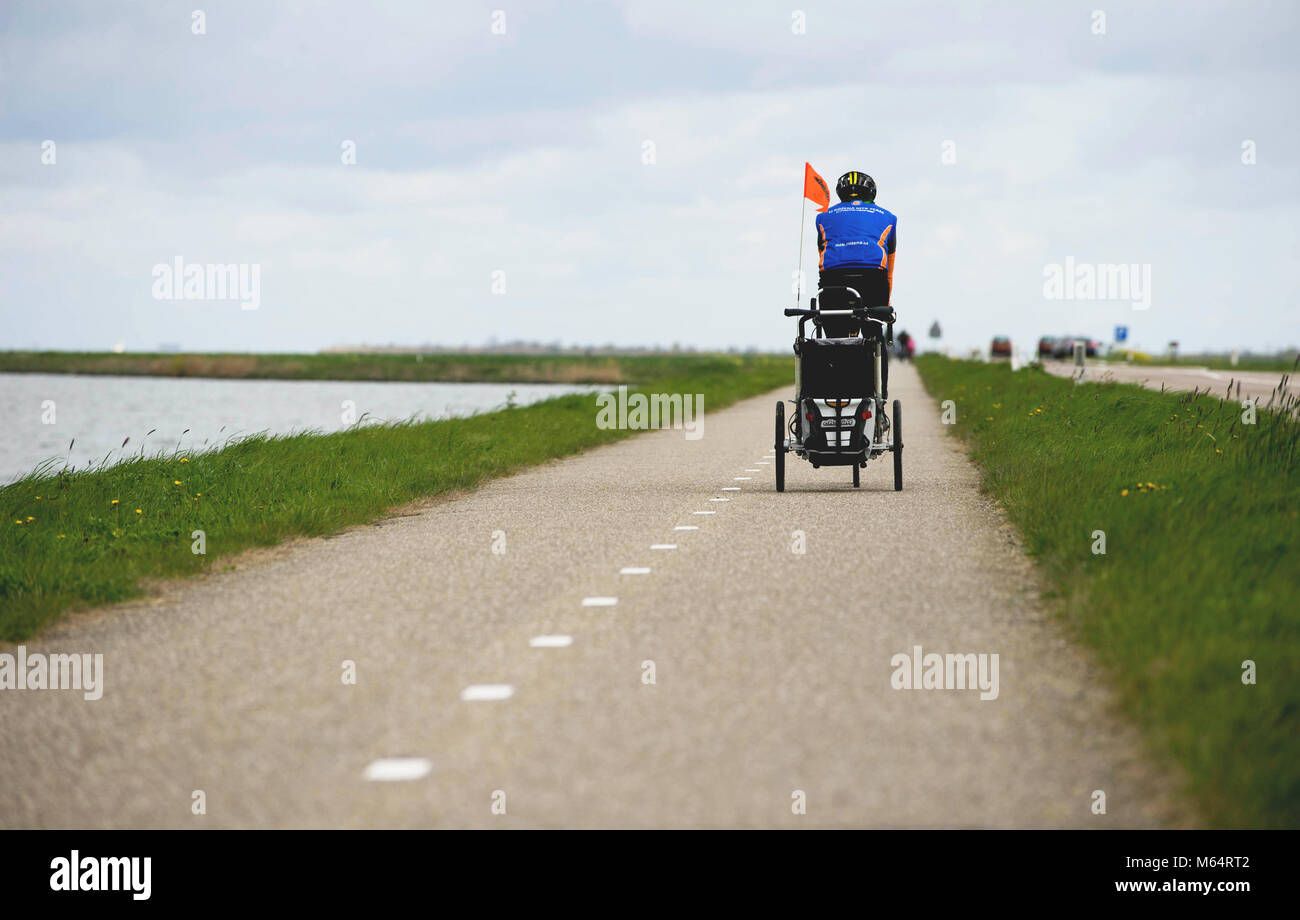 AMSTERDAM, NETHERLANDS, April 2017: Man on the Bike Pulling Baby Cart for a Bicycle. Bicycle path with Lake on One Site and the Motor Road on the Othe Stock Photo