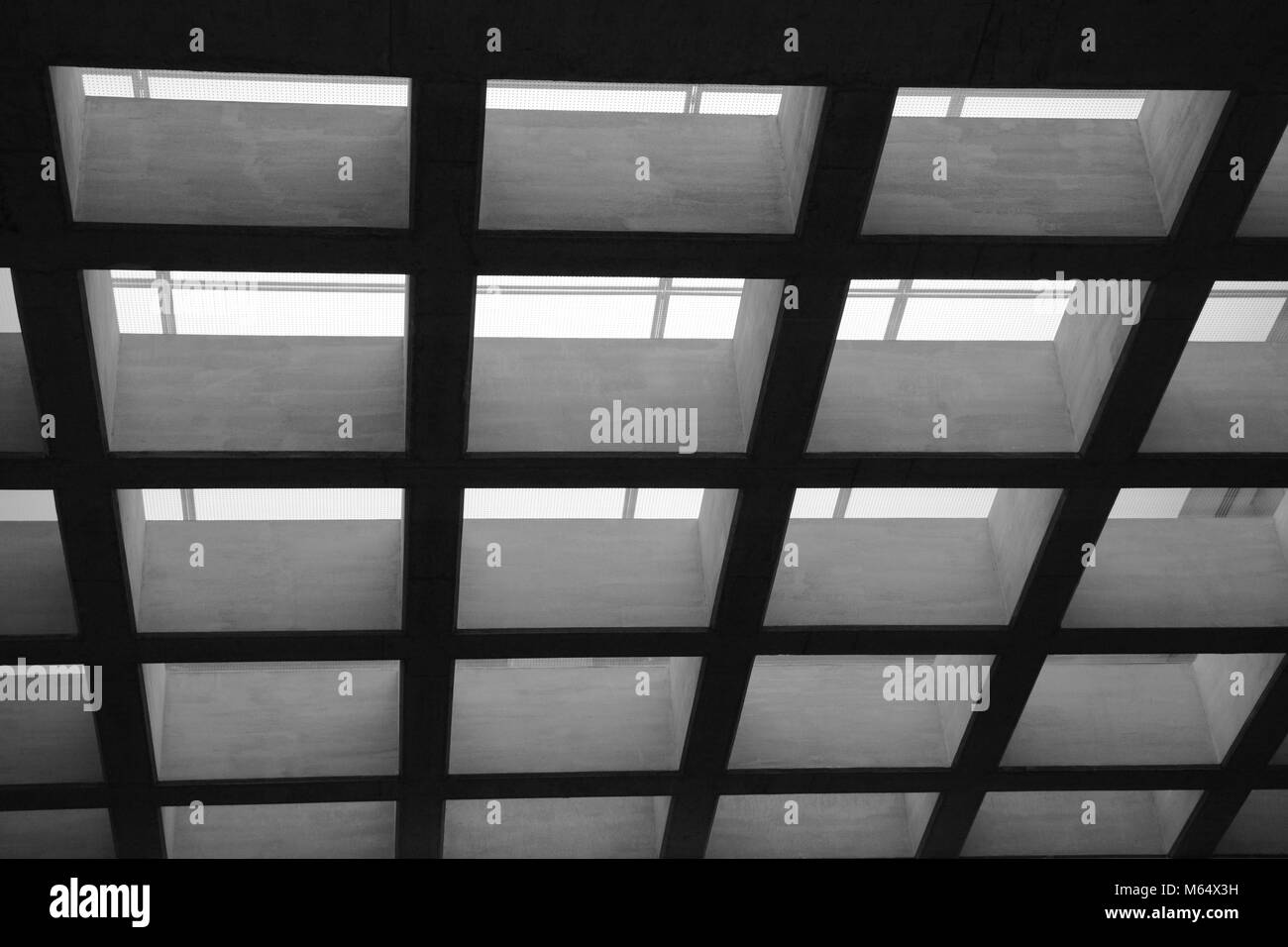 View looking up inside a building to a square patterned ceiling in mono Stock Photo