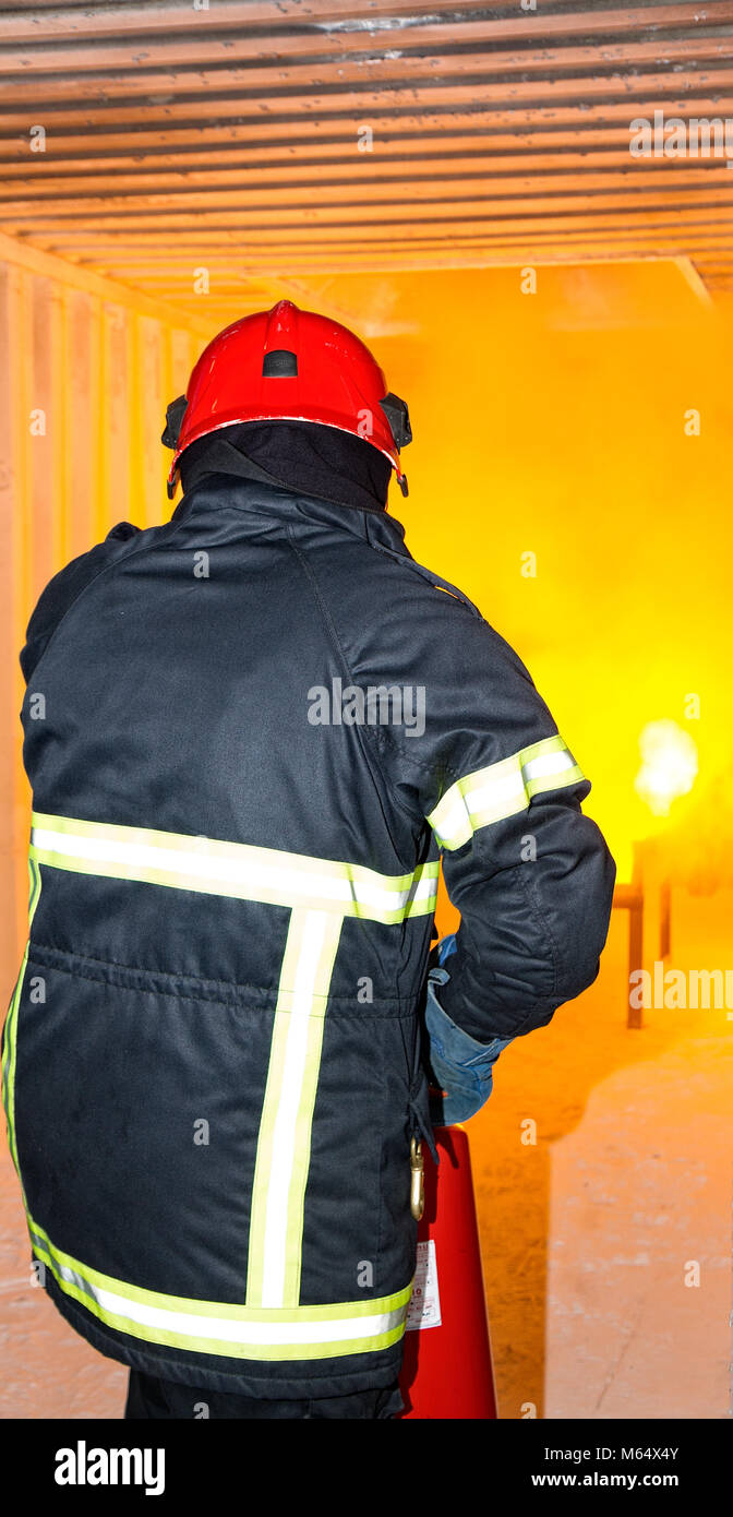 Fireman during training. Fire extinguisher. Golden yellow flames / fire in the background. Red helmet. Stock Photo