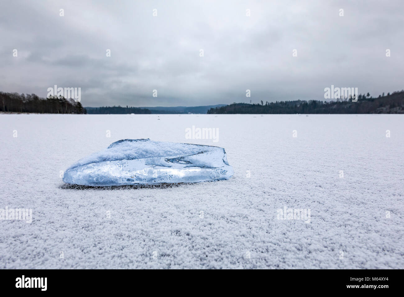 Low angle view of block of clear ice with a blue tint on top of snow and ice covered lake set againt dark winter landscape scenic  Model Release: No. Property Release: No. Stock Photo