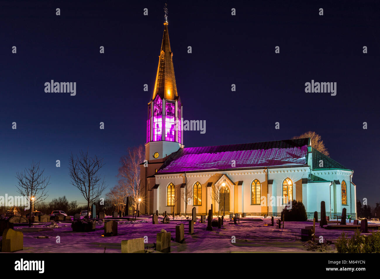 FLODA, SWEDEN - FEBRUARY 22 2018: Beautiful exterior view of swedish Skallsjö Church with the steeple lit up in predominantly purple at night in Floda, Lerum Municipality, Sweden  Model Release: No. Property Release: No. Stock Photo
