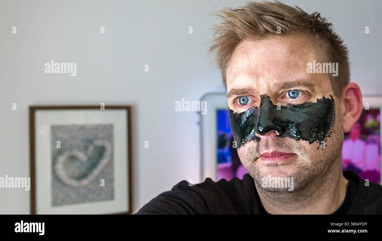 Mid adult caucasian man wearing black skincare face mask on his face looking away  Model Release: Yes.  Property Release: Yes (image on wall in background). Stock Photo