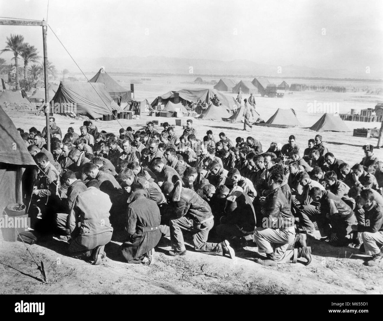 1940s U.S. ARMY SOLDIERS ATTEND CHURCH SERVICES ON A TROPICAL BEACH - a3739 HAR001 HARS HIGH ANGLE ADVENTURE RELIGIOUS COURAGE EXCITEMENT WORLD WAR TWO SUPPORT TENTS ARMED FORCE ATTEND FAITH MALES B&W BLACK AND WHITE CAUCASIAN ETHNICITY KNEEL OLD FASHIONED PERSONS Stock Photo