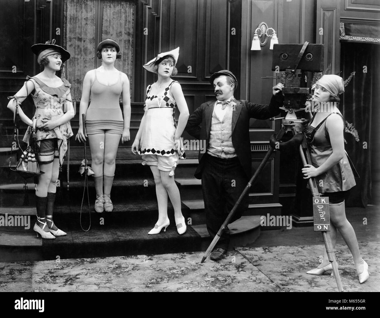 1910s COMIC PHOTOGRAPHER WITH MODELS IN SKIMPY BATHING COSTUMES SILENT MOVIE STILL - asm00721 CAM001 HARS 18-19 YEARS POSING SILENT 1910s COMEDY SILENT MOVIE SMALL GROUP OF PEOPLE BATHING SUIT SILENT MOVIE STILL MALES MID-ADULT WOMAN MOVIE CAMERA YOUNG ADULT WOMAN B&W BATHING BEAUTIES BEN TURPIN BLACK AND WHITE CAUCASIAN ETHNICITY HORIZONTAL MACK SENNETT OLD FASHIONED PERSONS SKIMPY STILL ACTRESS Stock Photo