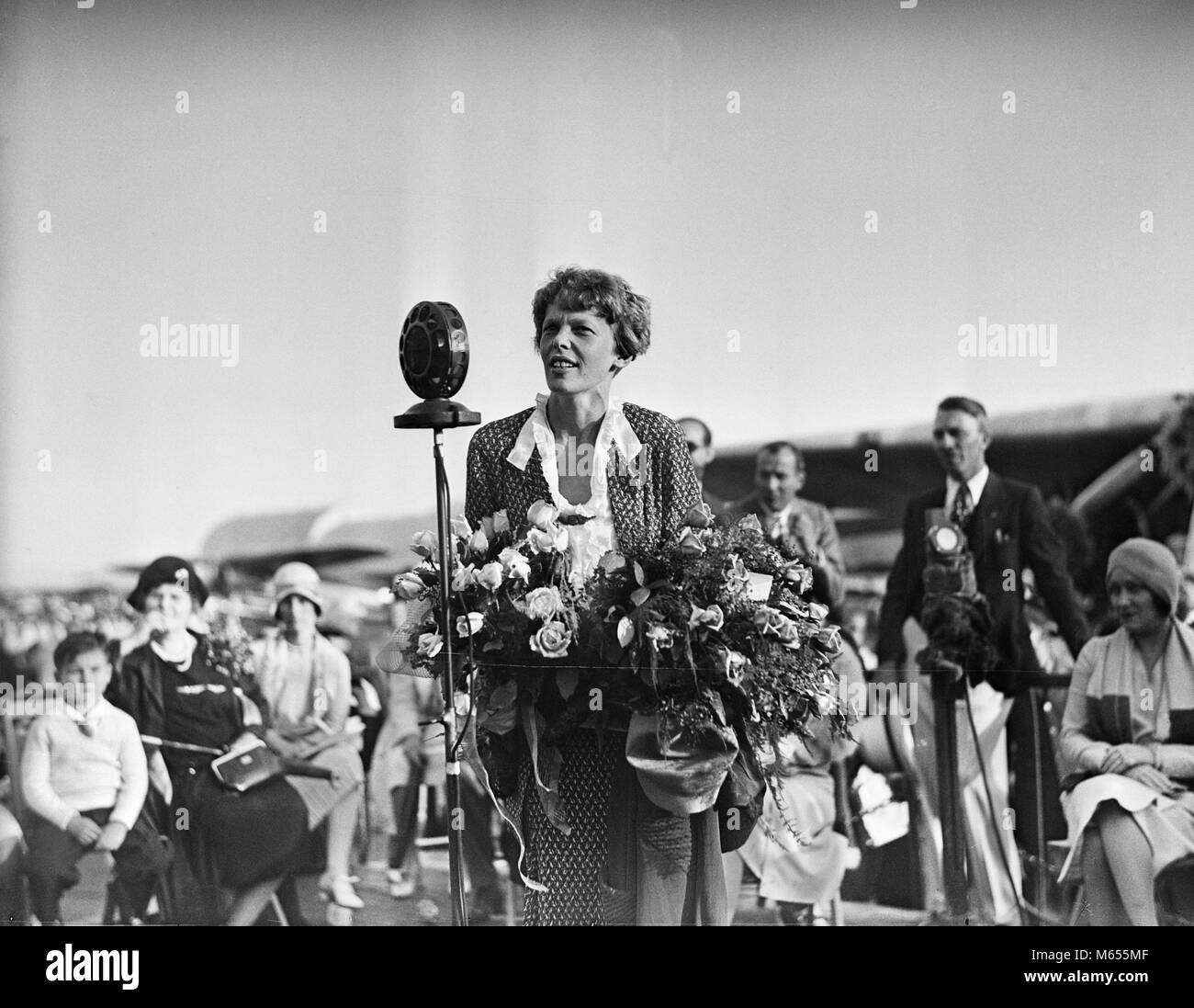 1920s 1929 AVIATOR AVIATRIX AMELIA EARHART SPEAKING TO CROWD HOLDING BOUQUET OF FLOWERS - asp gp74 ASP001 HARS B&W BLACK AND WHITE CAUCASIAN ETHNICITY EARHART GLENDALE AIRPORT JULY 7 OCCUPATIONS OLD FASHIONED PERSONS PUBLIC SPEAKING Stock Photo