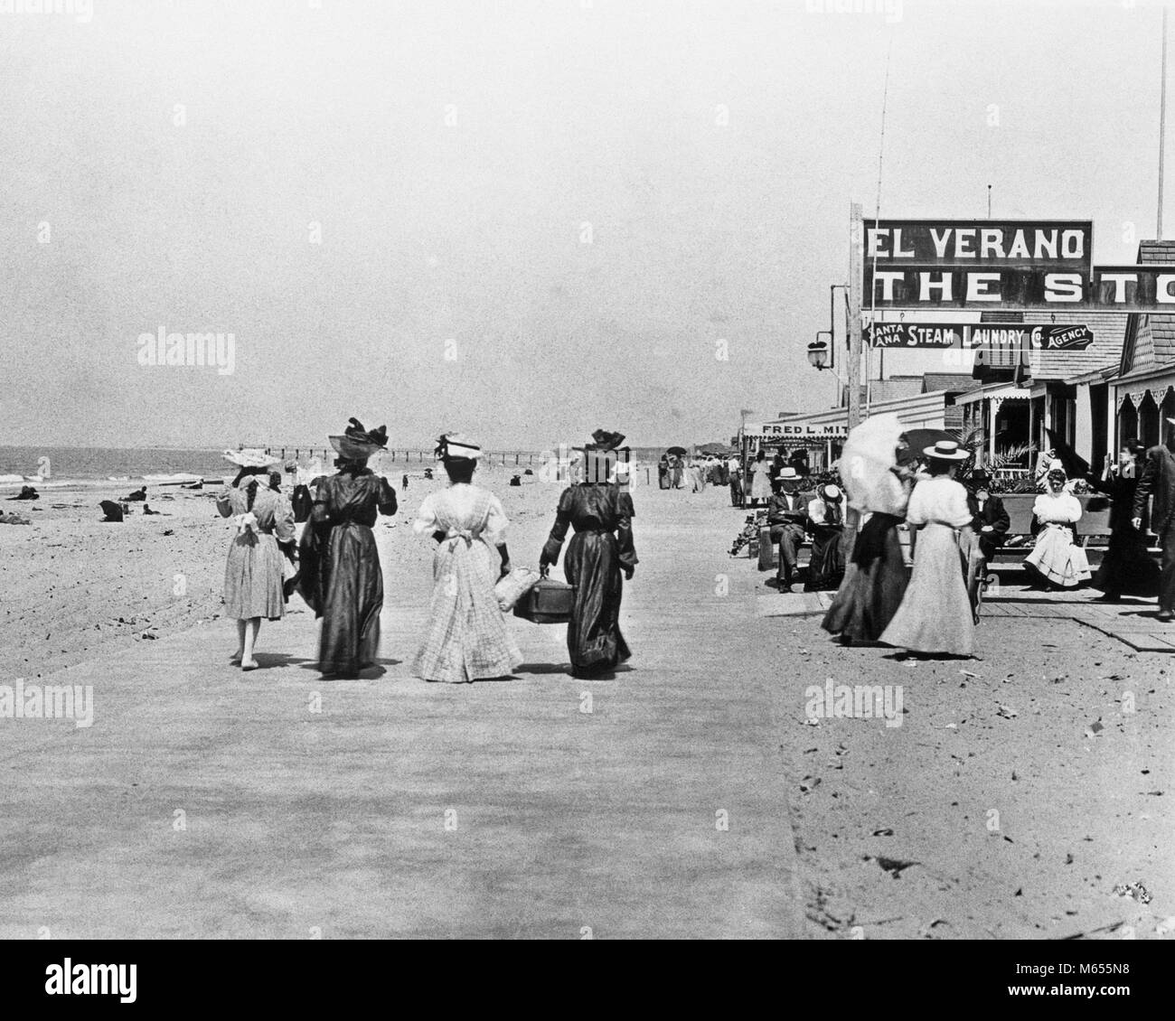 1910s 1912 PEOPLE STROLLING AWAY ON PAVED WALK ALONG BEACH NEWPORT BEACH CALIFORNIA USA - asp hp5396 ASP001 HARS BOARDWALK LEISURE STYLES RELAXATION ALONG RECREATION SEASIDE 1890s BEACHES FASHIONS WEST COAST ESCAPE STOREFRONT GROUP OF PEOPLE TURN OF CENTURY JUVENILES PACIFIC OCEAN 1912 B&W BLACK AND WHITE COASTAL LONG SKIRTS NEWPORT NEWPORT BEACH OLD FASHIONED PERSONS SOUTHERN CALIFORNIA Stock Photo