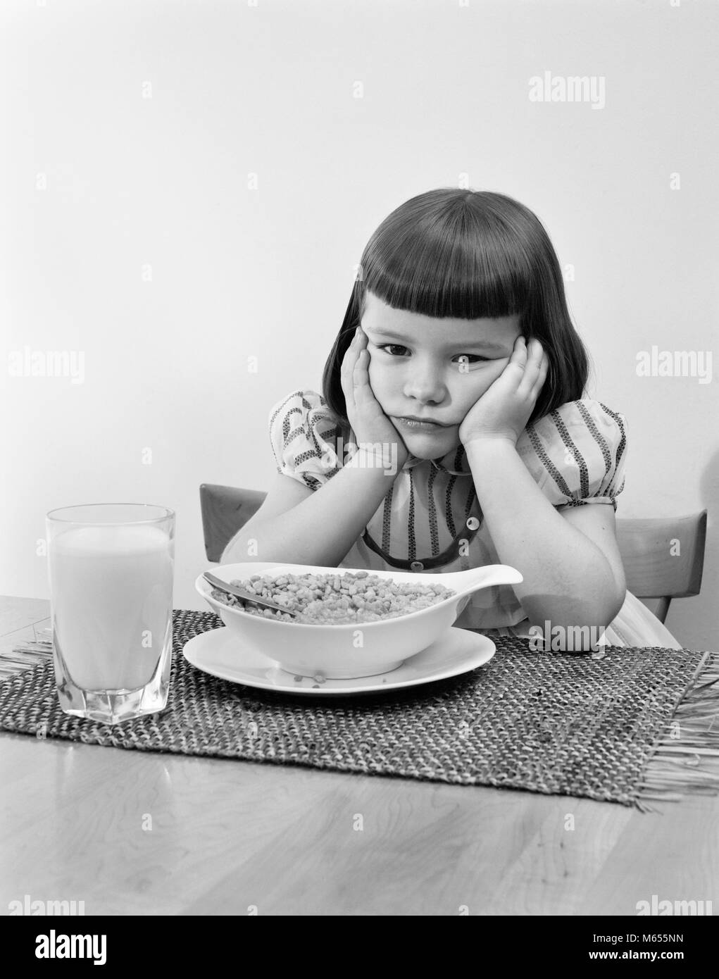 1950s GRUMPY GIRL SITTING AT TABLE WITH BOWL OF CEREAL GLASS OF MILK LEANING CHIN ON HANDS - asp x16630 CAM001 HARS INDOORS NOSTALGIA SADNESS EYE CONTACT 3-4 YEARS BRUNETTE 5-6 YEARS AILING JUVENILES MISERABLE AVERSION B&W BANGS BLACK AND WHITE CAUCASIAN ETHNICITY DISLIKE DISPLEASED HATE OLD FASHIONED UNAPPETIZING UNHAPPINESS UNWELL Stock Photo