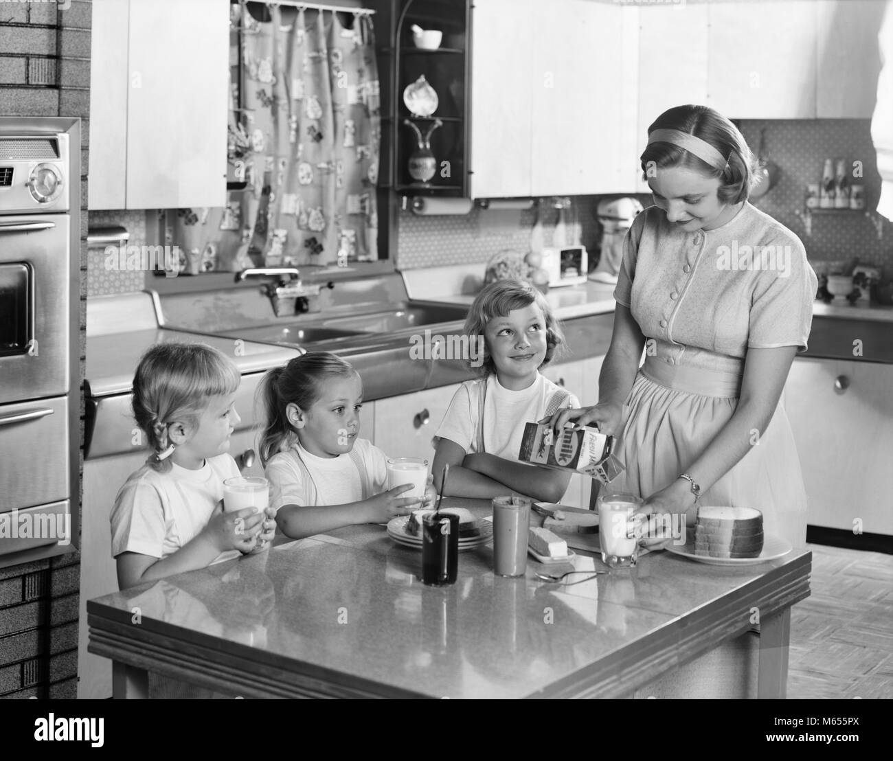 1950s MOTHER THREE DAUGHTERS STANDING AROUND KITCHEN TABLE MAKING LUNCH PEANUT BUTTER JELLY SANDWICHES MOTHER POURING GLASS MILK - asp x16745 CAM001 HARS JUVENILE BLOND FRIEND SANDWICHES CAUCASIAN FEMALES HEALTHINESS HOME LIFE COPY SPACE FRIENDSHIP HALF-LENGTH LADIES DAUGHTERS CARING BUTTER INDOORS SIBLINGS SISTERS NOSTALGIA TOGETHERNESS 30-35 YEARS 35-40 YEARS 7-9 YEARS HOMEMAKER 5-6 YEARS HAPPINESS HOMEMAKERS MOMS GROWTH HOUSEWIVES PEANUT SIBLING SMALL GROUP OF PEOPLE JUVENILES MID-ADULT MID-ADULT WOMAN B&W BLACK AND WHITE CAUCASIAN ETHNICITY JELLY OLD FASHIONED PBJ PEANUT BUTTER PERSONS Stock Photo