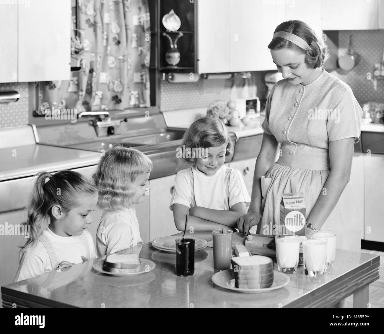 1950s MOTHER & THREE DAUGHTERS STANDING AT KITCHEN TABLE MAKING LUNCH PEANUT BUTTER & JELLY SANDWICHES & GLASSES OF MILK - asp x16746 CAM001 HARS SISTER 1 JUVENILE BLOND FRIEND SANDWICHES CAUCASIAN FEMALES HEALTHINESS HOME LIFE COPY SPACE FRIENDSHIP HALF-LENGTH LADIES DAUGHTERS CARING BUTTER INDOORS SIBLINGS SISTERS NOSTALGIA TOGETHERNESS 30-35 YEARS 35-40 YEARS 7-9 YEARS HOMEMAKER 5-6 YEARS HAPPINESS HOMEMAKERS MOMS GROWTH HOUSEWIVES PEANUT SIBLING SMALL GROUP OF PEOPLE JUVENILES MID-ADULT MID-ADULT WOMAN B&W BLACK AND WHITE CAUCASIAN ETHNICITY JELLY OLD FASHIONED PBJ PEANUT BUTTER PERSONS Stock Photo