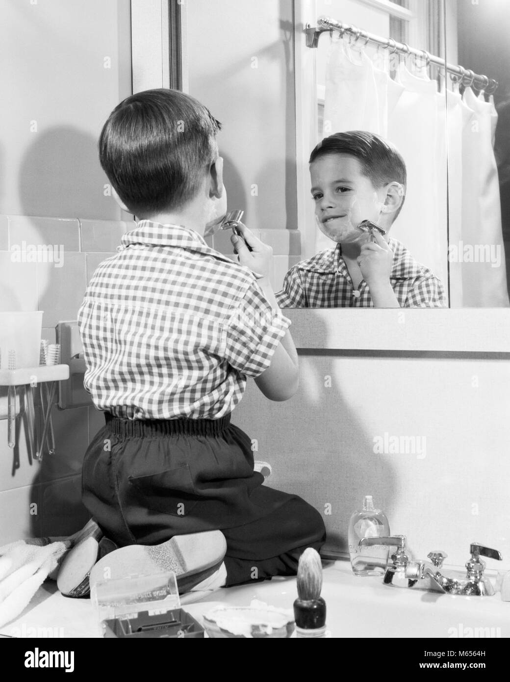1950s BOY KNEELING BATHROOM SINK TRYING TO SHAVE HIS BEARD LIKE FATHER LIKE SON - bj002472 CAM001 HARS BRUNETTE KNEELING 5-6 YEARS HIS SHAVE TRYING VERTICAL FACIAL HAIR GROWTH LIKE BEHAVIOR JUVENILES MALES B&W BLACK AND WHITE CAUCASIAN ETHNICITY DATED IMITATION OLD FASHIONED OLD-FASHIONED PERSONS SINGLE BOY IN Stock Photo