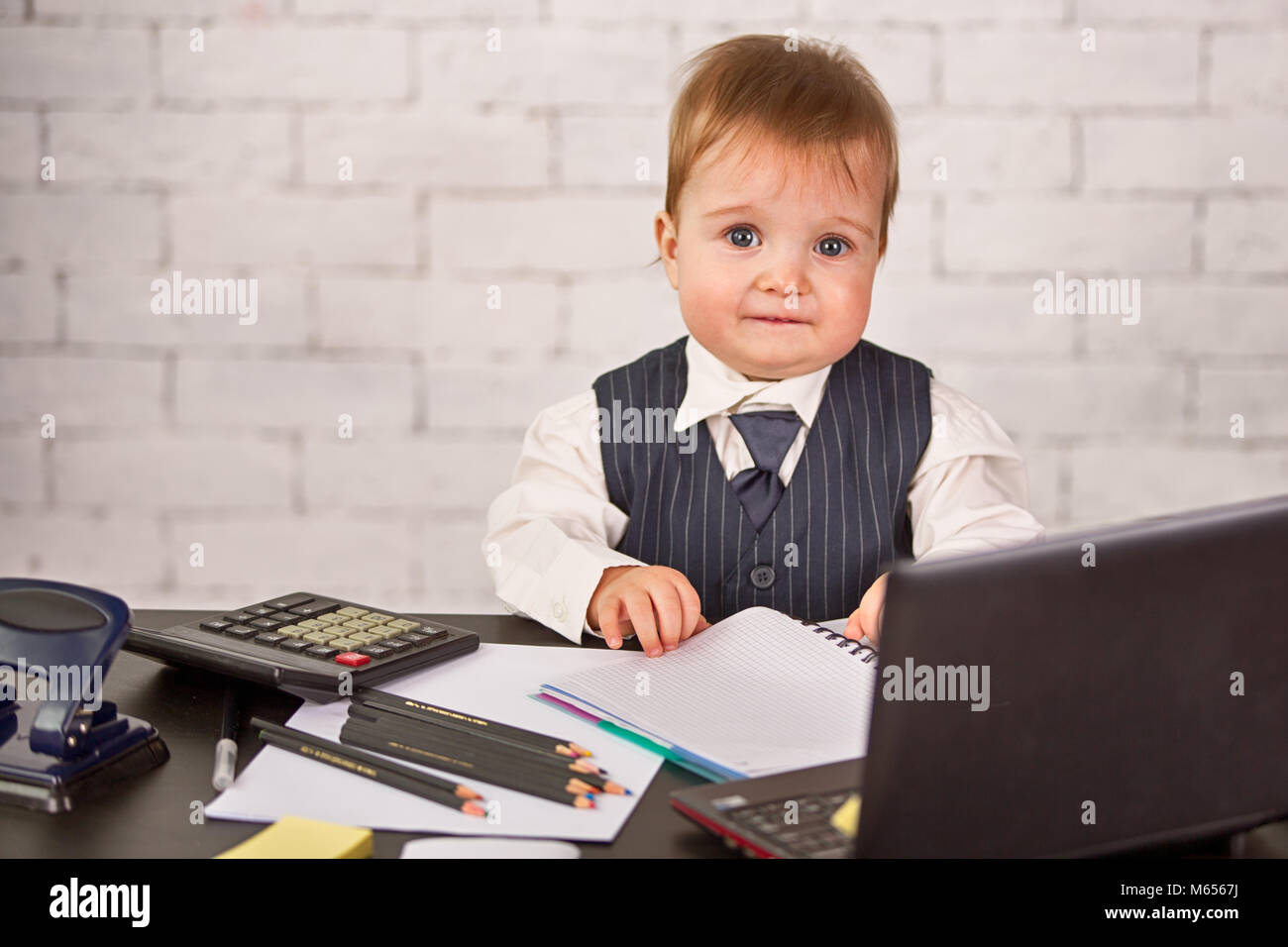 A Cute Blond Child In A Business Suit Is Sitting At The Desk