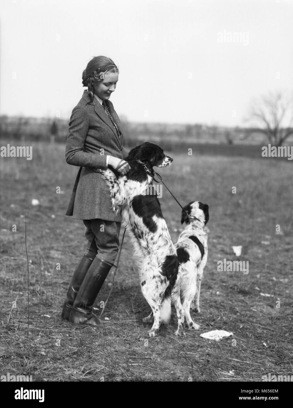 1920s SMILING WOMAN WEARING WOOL COAT JODHPURS LEATHER BOOTS STANDING PLAYING WITH TWO ENGLISH SETTER DOGS - d3309 HAR001 HARS ONE PERSON ONLY LUXURY WOOL COPY SPACE FRIENDSHIP FULL-LENGTH LADIES ANIMALS HUNTER ENGLISH NOSTALGIA TOGETHERNESS 20-25 YEARS HAPPINESS TWO ANIMALS MAMMALS STYLES CANINES 18-19 YEARS FALL SEASON SMILES SPOTS CONNECTION JOYFUL FASHIONS COOPERATION SPOTTED CANINE HIND HUNTING DOGS HUNTRESS JODHPURS MAMMAL SETTER YOUNG ADULT WOMAN B&W BLACK AND WHITE CAUCASIAN ETHNICITY OLD FASHIONED PERSONS Stock Photo