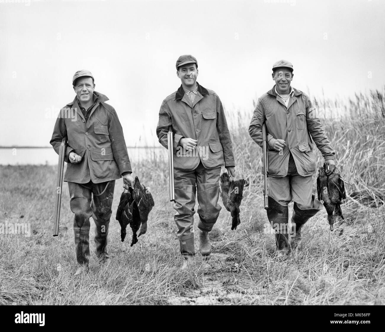 1950s THREE MEN LOOKING AT CAMERA HOLDING SHOTGUNS WALKING THROUGH GRASSY WETLANDS EACH CARRYING BRACE OF DUCKS - d3634 HAR001 HARS HAPPINESS CHEERFUL ADVENTURE RELAXATION EXCITEMENT EXTERIOR RECREATION TRIO PRIDE SMILES JOYFUL COOPERATION GRASSY SMALL GROUP OF ANIMALS SMALL GROUP OF PEOPLE FIREARM FIREARMS HUNTERS MALES MID-ADULT MID-ADULT MAN SHOTGUNS WETLANDS B&W BLACK AND WHITE BRACE CAUCASIAN ETHNICITY DOUBLE BARREL LOOKING AT CAMERA OLD FASHIONED PERSONS Stock Photo