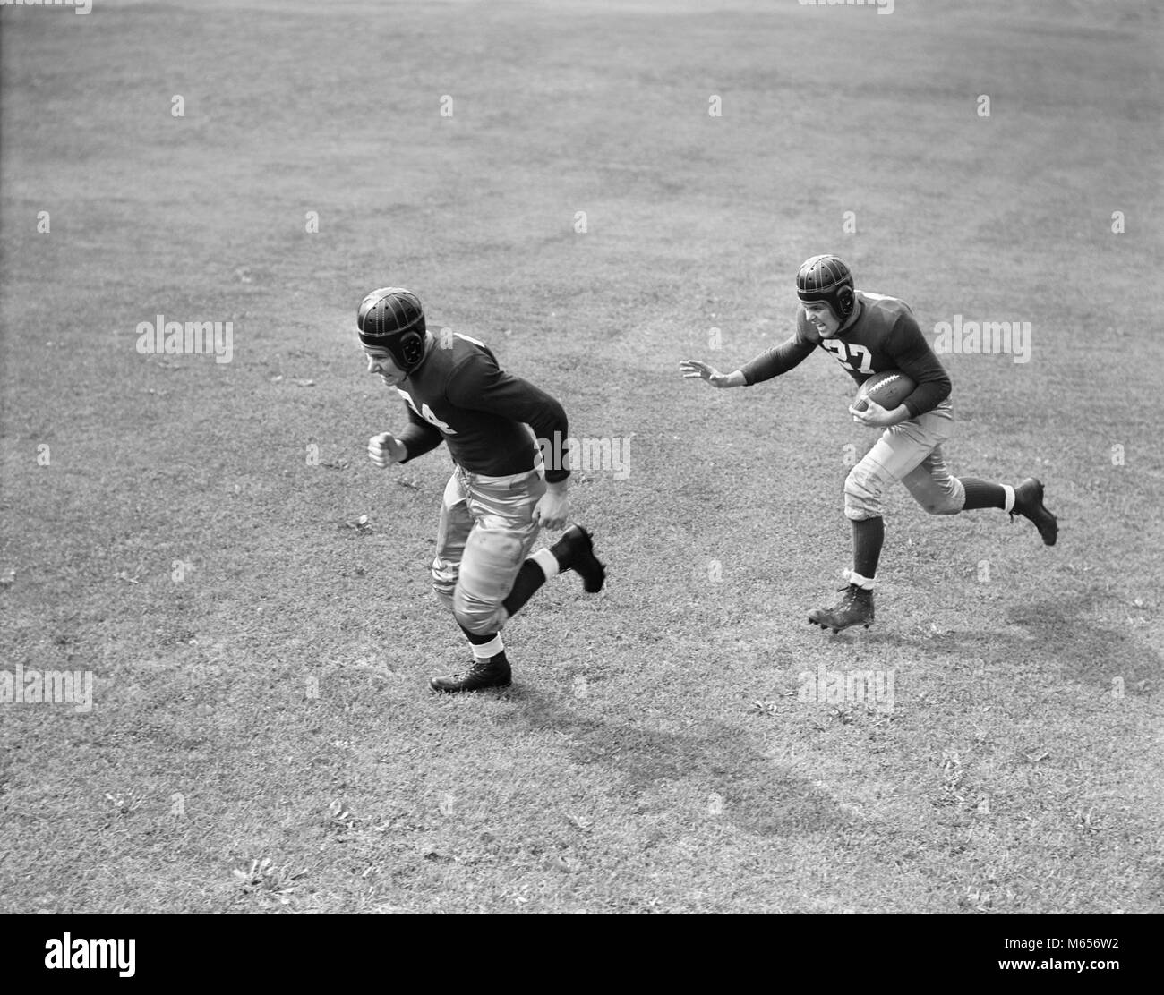 1940s TWO MEN PLAYING FOOTBALL WEARING LEATHER HELMETS ONE RUNNING WITH FOOTBALL OTHER BLOCKING FOR HIM - f9632 HAR001 HARS HEALTHINESS COPY SPACE FULL-LENGTH PHYSICAL FITNESS RISK ATHLETIC PROFESSION TOWARDS CONFIDENCE NOSTALGIA TOGETHERNESS 20-25 YEARS GOALS OCCUPATION PROTECTING HIGH ANGLE PROTECTION STRENGTH STRATEGY UNIVERSITIES CAREERS EXCITEMENT RECREATION 18-19 YEARS DIRECTION SUPPORT CONNECTION HIGHER EDUCATION SPORTS FOOTBALL GOOD HEALTH ATHLETES BLOCKING COLLEGES HELMETS BALL SPORT DEFENSE MALES YOUNG ADULT MAN AMERICAN FOOTBALL B&W BLACK AND WHITE CAUCASIAN ETHNICITY INTERFERENCE Stock Photo