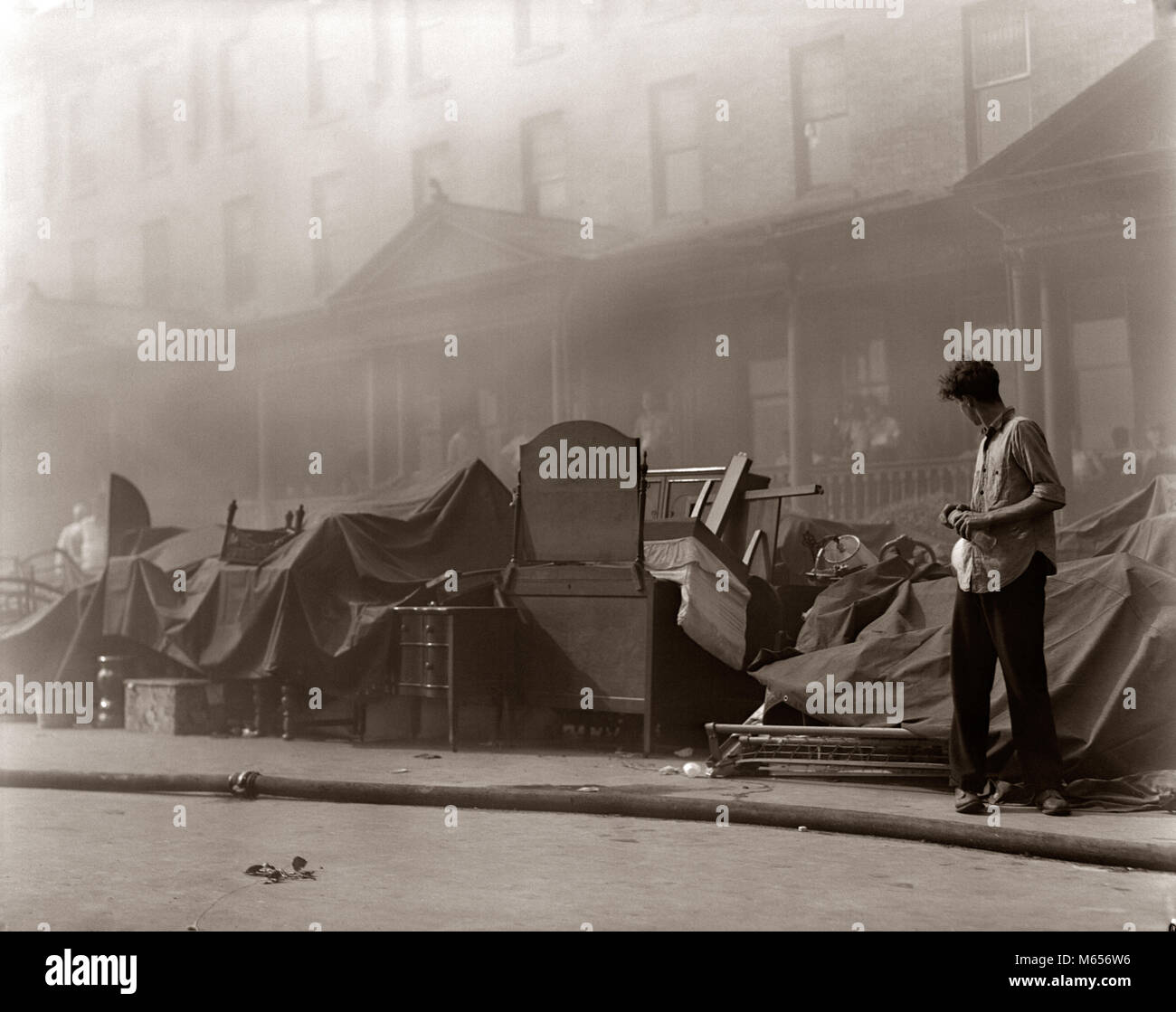 1930s 1940s YOUNG MAN LOOKING AT FURNITURE STACKED ON SIDEWALK IN FRONT OF ROW HOUSE PARTIALLY OBSCURED BY SMOKE FROM FIRE - f9645 HAR001 HARS NOSTALGIA STACKED 20-25 YEARS YOUNGSTER DISASTER DANGEROUS PROTECTION EXTERIOR LOW ANGLE EVICTION OCCASION 18-19 YEARS RISKY ONE PERSON WITH OTHERS CONCEPTUAL PEOPLE OCCUPATIONS LARGE GROUP OF OBJECTS PARTIALLY YOUNG ADULT MAN B&W BELONGINGS BLACK AND WHITE DAMAGE EVACUATION FIRE DEPARTMENT OBSCURED OLD FASHIONED PERSONS RESIDENT Stock Photo