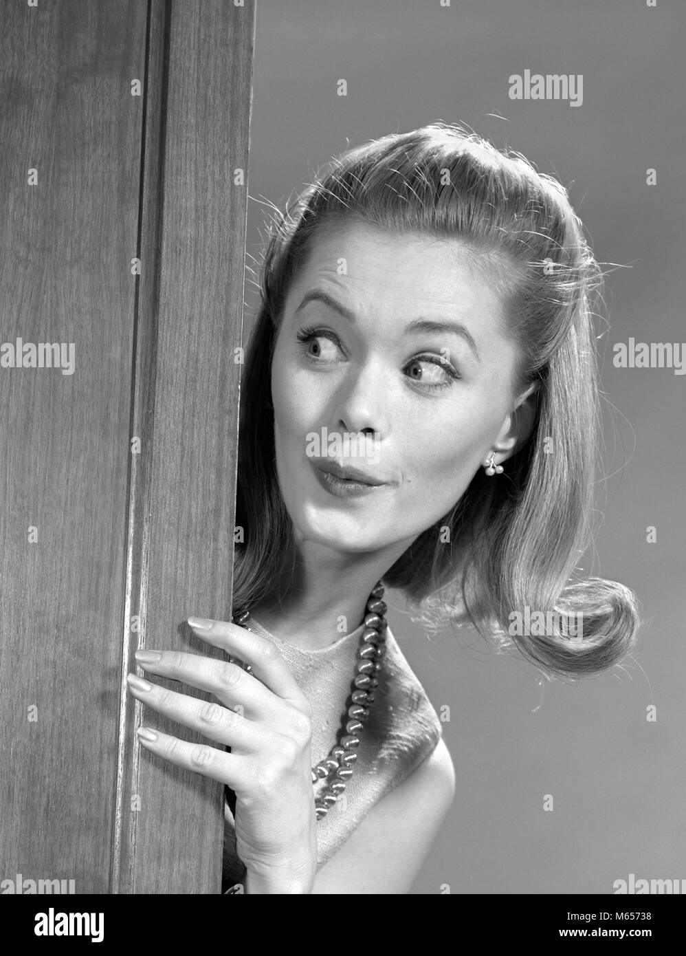 1960s WOMAN PEEKING AROUND DOOR WITH FUNNY FACIAL EXPRESSION - g6952 HAR001 HARS LIFESTYLE FLIP FEMALES STUDIO SHOT GROWNUP ONE PERSON ONLY HOME LIFE COPY SPACE LADIES GROWN-UP INDOORS NOSTALGIA SNOOPING 20-25 YEARS 25-30 YEARS HUMOROUS HAPPINESS HEAD AND SHOULDERS DISCOVERY HAIRSTYLE KNOWLEDGE OPPORTUNITY VOYEUR SPYING SNOOP EAVESDROPPING MID-ADULT MID-ADULT WOMAN PEOPLE ADULTS B&W BLACK AND WHITE CAUCASIAN ETHNICITY NOSY OLD FASHIONED PERSONS Stock Photo