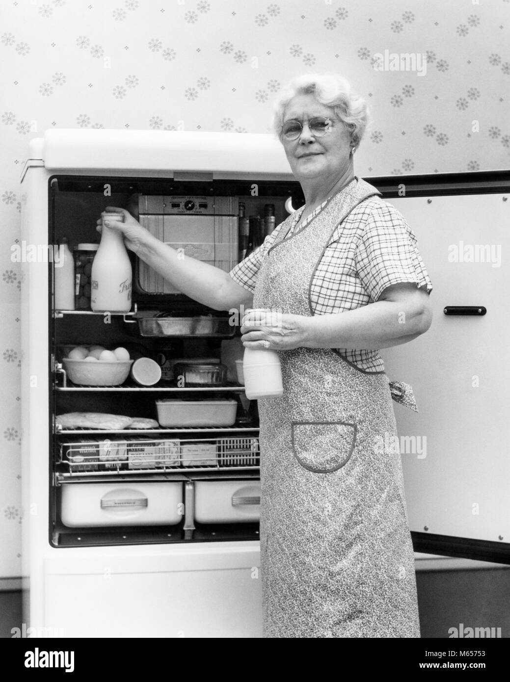1930s 1940s SENIOR WOMAN HOUSEWIFE GRANDMOTHER LOOKING AT CAMERA TAKING TWO GLASS BOTTLES OF MILK OUT OF KITCHEN REFRIGERATOR - h5891 HAR001 HARS FULL-LENGTH HALF-LENGTH LADIES INDOORS CONFIDENCE SENIOR ADULT NOSTALGIA MIDDLE-AGED SENIOR WOMAN 50-55 YEARS 55-60 YEARS 60-65 YEARS MIDDLE-AGED WOMAN OLDSTERS OLDSTER CHOICE PRIDE ELDERS B&W BLACK AND WHITE CAUCASIAN ETHNICITY LOOKING AT CAMERA OLD FASHIONED PERSONS PLACING TAKING FROM Stock Photo