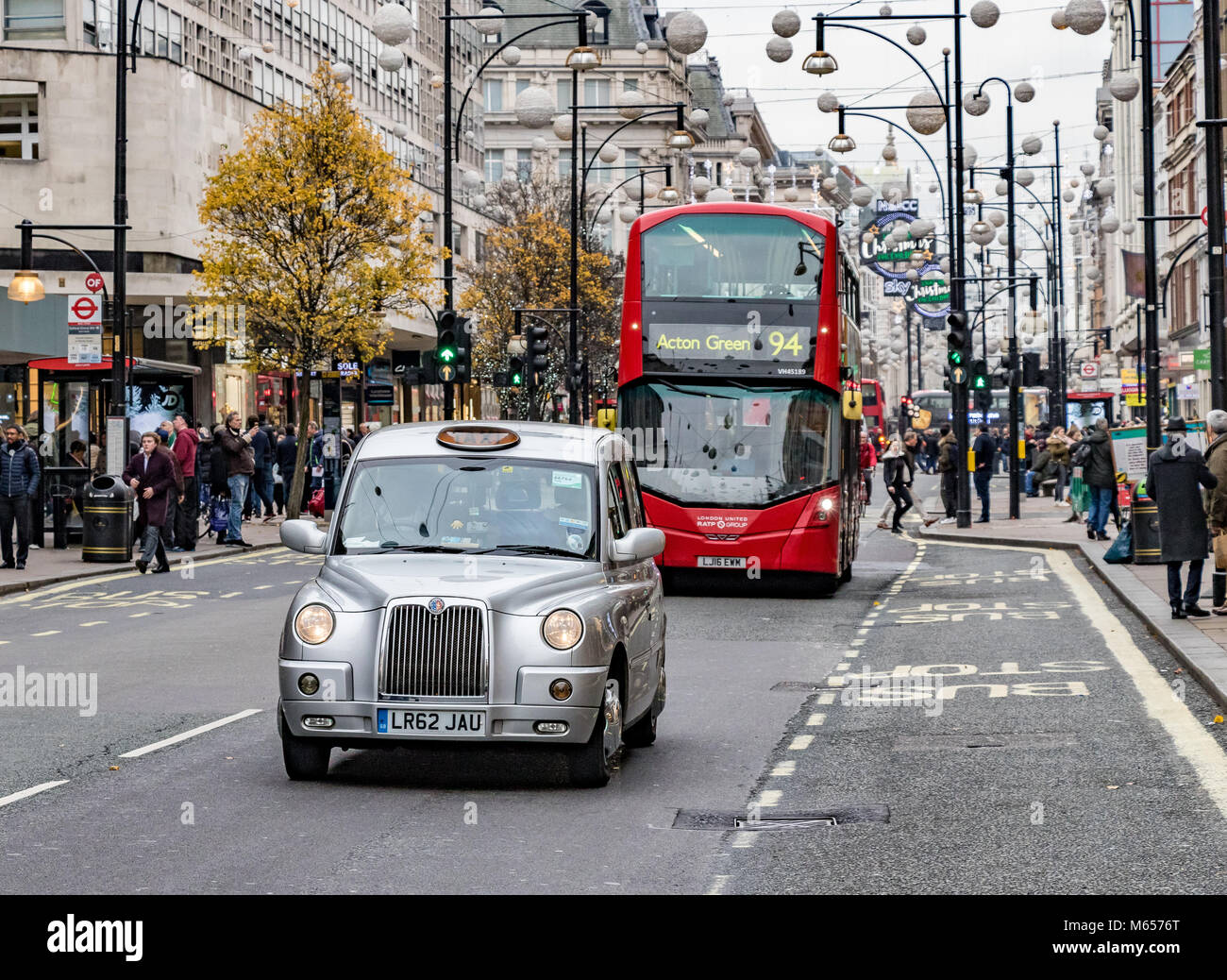 A silver London taxi and a No94 London Bus moving along Oxford Street, London, UK Stock Photo