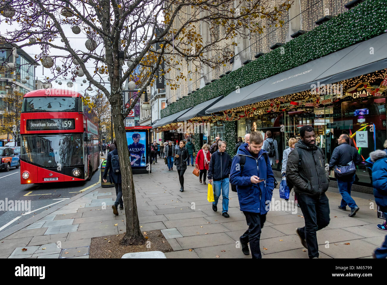 A man checks his mobile phone as a No 159 Bus to Streatham , pulls up at a Bus stop on Oxford Street, busy with shoppers ,Oxford St, London ,UK Stock Photo