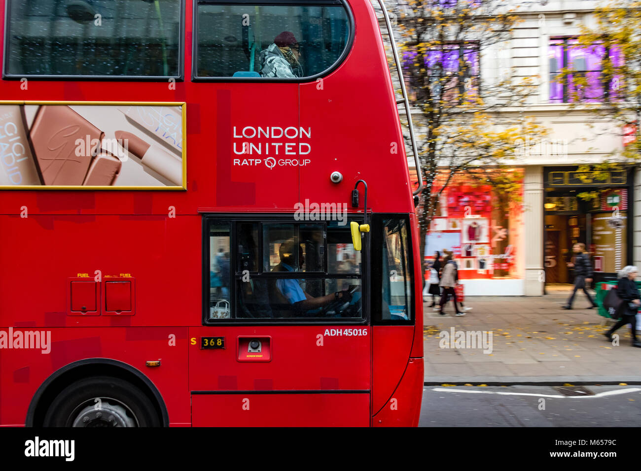 London Bus Driver in his cab driving along Oxford Street while a man sitting on The top deck at the front listens to headphones ,Oxford St , London,UK Stock Photo