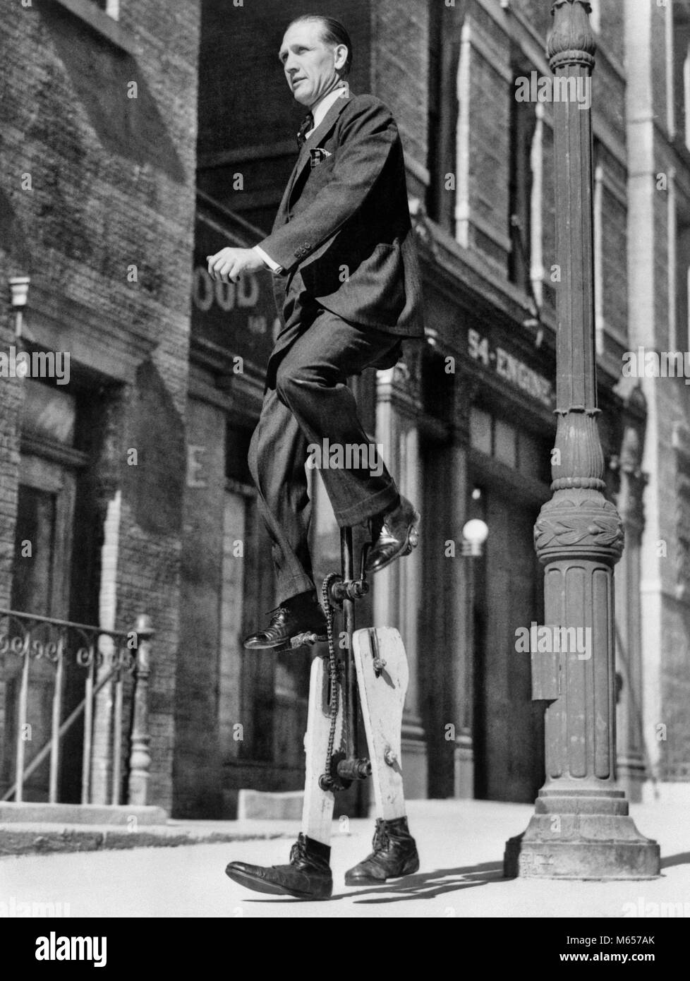 1930s INVENTOR WALTER NILSSON SITTING ON UNICYCLE WHILE WALKING TO WORK ON STILTS LOS ANGELES