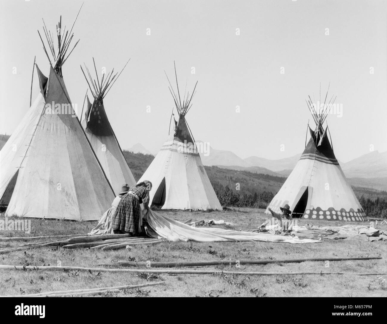 1920s THREE NATIVE AMERICAN INDIAN WOMEN OF SIOUX TRIBE WORKING ON TEPEE POLES AND HIDES MONTANA USA - i355 HAR001 HARS 30-35 YEARS GOALS NORTH AMERICAN POLES TIPI EXTERIOR SUPPORT TEPEE COOPERATION TRIBE MT NATIVE AMERICAN ROCKY MOUNTAINS SMALL GROUP OF PEOPLE CONICAL MID-ADULT MID-ADULT WOMAN NATIVE AMERICANS B&W BLACK AND WHITE CONE SHAPE HIDES INDIGENOUS OLD FASHIONED PERSONS Stock Photo