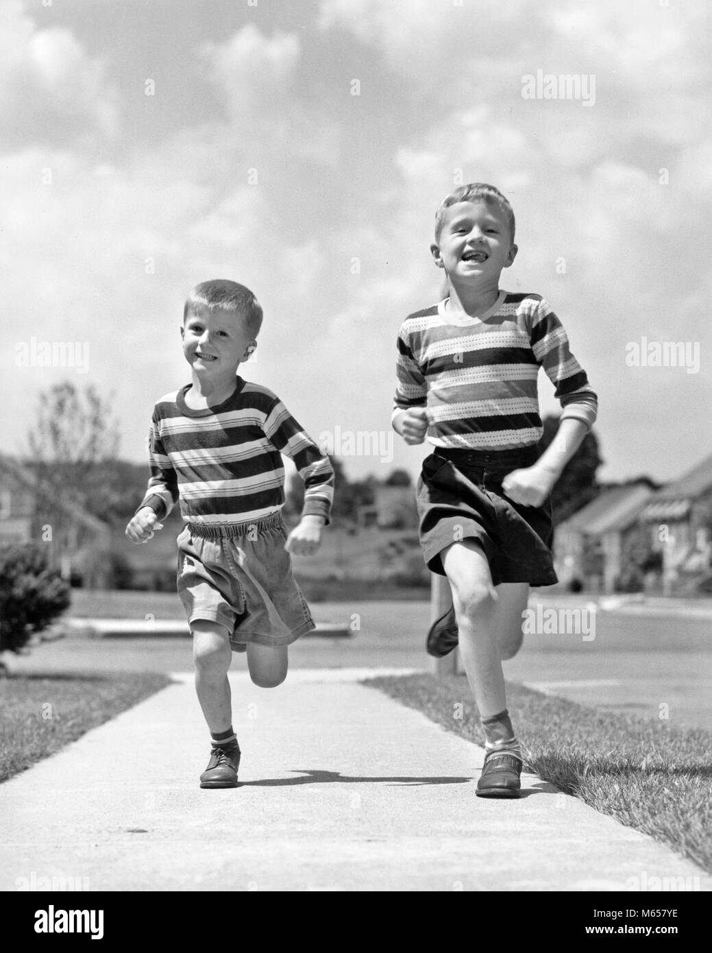 1950s TWO SMILING BOYS BROTHERS WEARING STRIPED SHIRTS SHORTS RUNNING ON SIDEWALK LOOKING AT CAMERA SUBURBAN NEIGHBORHOOD - j1442 HAR001 HARS FULL-LENGTH PHYSICAL FITNESS SIBLINGS NOSTALGIA TOGETHERNESS SUMMERTIME EYE CONTACT 7-9 YEARS FREEDOM 5-6 YEARS HAPPINESS NEIGHBORHOOD CHEERFUL ADVENTURE EXCITEMENT RECREATION SHIRTS GROWTH SIBLING SMILES JOYFUL ESCAPE SHORT PANTS T-SHIRT JUVENILES MALES TEE SHIRT B&W BLACK AND WHITE CAUCASIAN ETHNICITY LOOKING AT CAMERA OLD FASHIONED Stock Photo