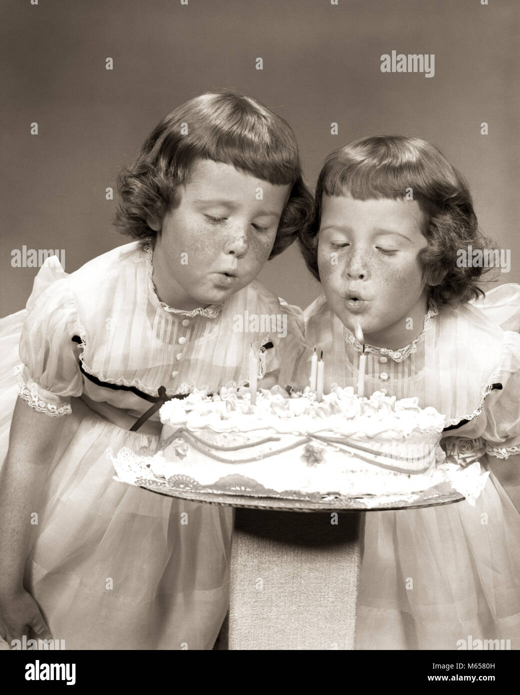 1950s TWIN GIRLS FRECKLES BLOWING OUT CANDLES BIRTHDAY CAKE - j2296 HAR001 HARS INDOORS FRECKLES SIBLINGS SISTERS WISHING NOSTALGIA TOGETHERNESS 3-4 YEARS MATCHING SAME 5-6 YEARS NOURISH GROWTH SIBLING CONNECTION COOPERATION NOURISHMENT WISH LOOK-ALIKE DRESS ALIKE DUPLICATE JUVENILES LOOK ALIKE B&W BANGS BLACK AND WHITE CAUCASIAN ETHNICITY CLONE FRECKLE-FACED IDENTITY OLD FASHIONED Stock Photo