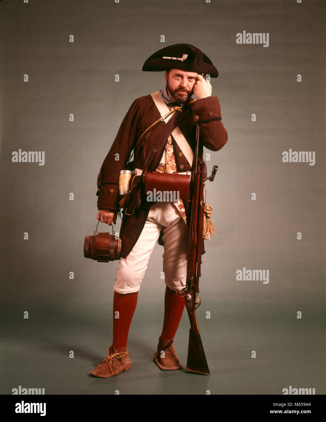 1970s 1776 AMERICAN REVOLUTION HISTORICAL REENACTOR MILITIA SOLDIER TRICORN HAT FLINTLOCK MUSKET AND BAYONET LOOKING AT CAMERA - kc6785 HAR001 HARS ONE PERSON ONLY UNITED STATES FULL-LENGTH RIFLE UNITED STATES OF AMERICA CHARACTER WHISKEY INDOORS ROUGH NOSTALGIA 20-25 YEARS 25-30 YEARS 30-35 YEARS HISTORIC SUCCESS PEOPLE STORY OCCUPATION ADVENTURE HOBBY LEISURE RELAXATION CHARACTERS HOBBIES KNOWLEDGE RECREATION TRICORN OCCASION FLINTLOCK PATRIOT UNIFORMS MUSKET REBELLION REENACTOR REENACTORS ARMED FORCE MUSKETS REENACTING WOOL COAT MALES MINUTEMAN PATRIOTS WHISKY BAYONET BAYONETS CARTRIDGE BOX Stock Photo