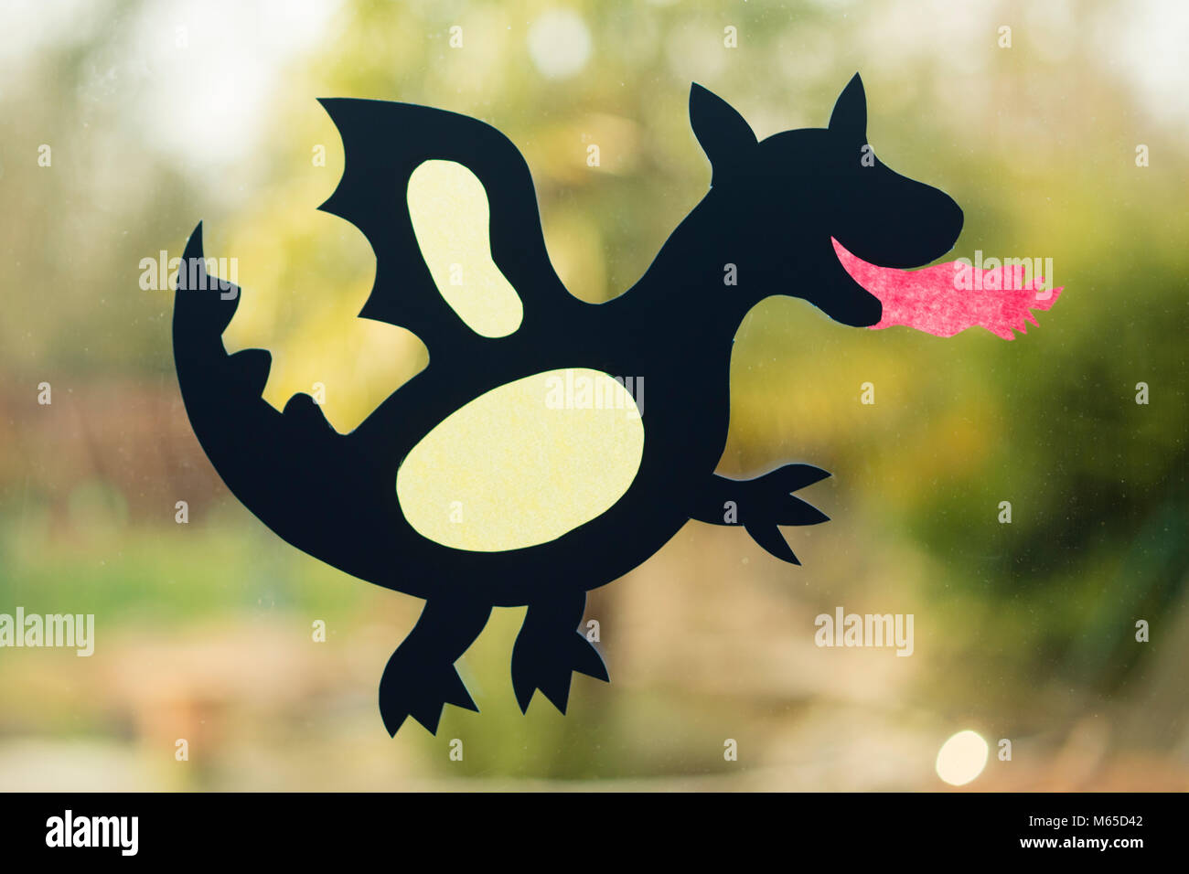 shape of a dragon made with paper as handicraft activity for children and placed on window glass. Stock Photo