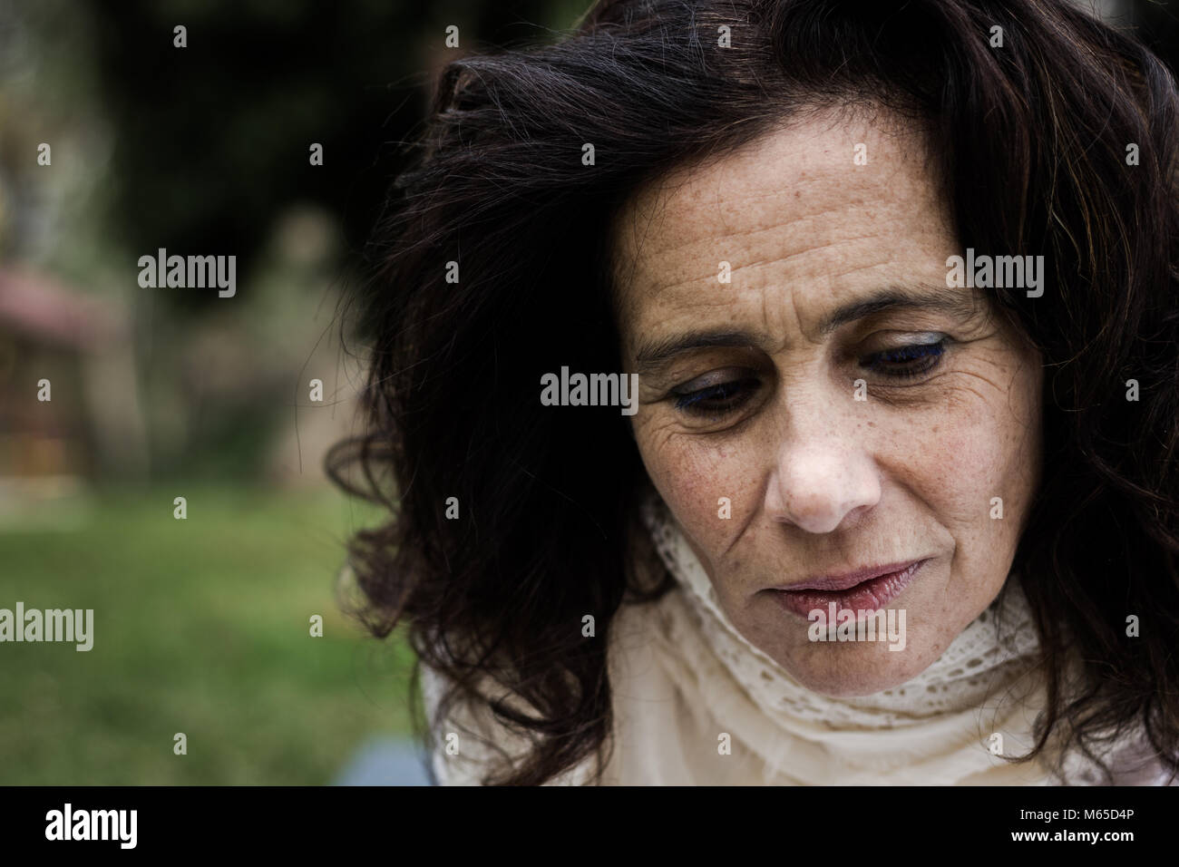 Sad look portrait of middle aged beautiful woman in the park. Concerned, depressed expression. Bad news, melancholy, pessimistic concept Stock Photo