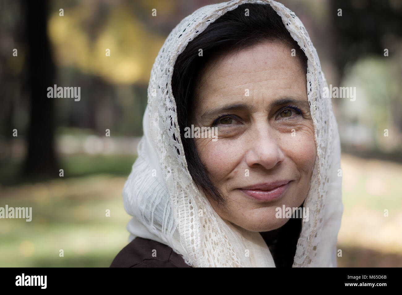 Portrait of mature woman covering her head with hijab style white shawl in the park. Young looking woman with white veil over head, Muslim look Stock Photo