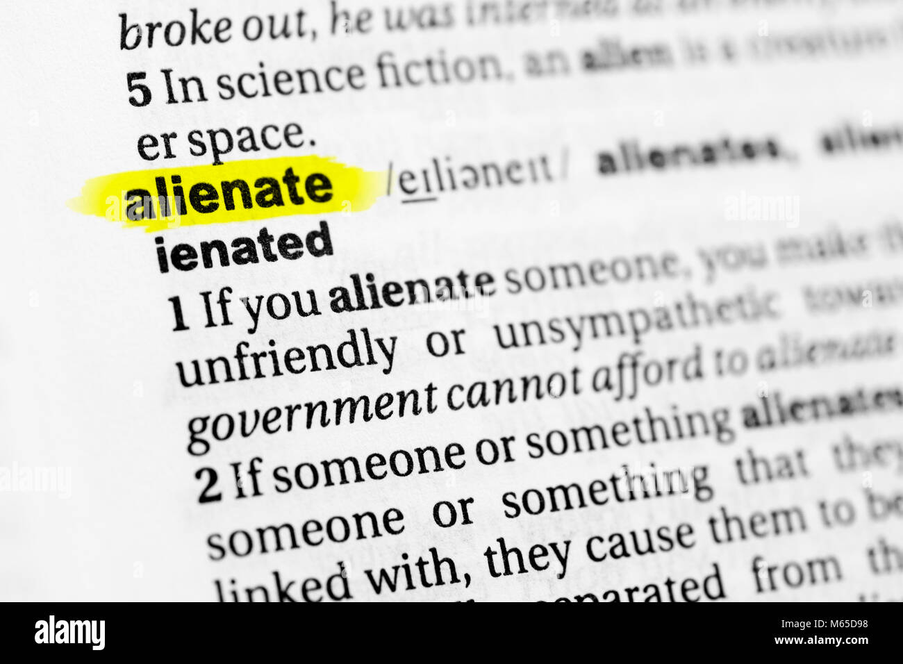 Highlighted English word "alienate" and its definition in the dictionary. Stock Photo