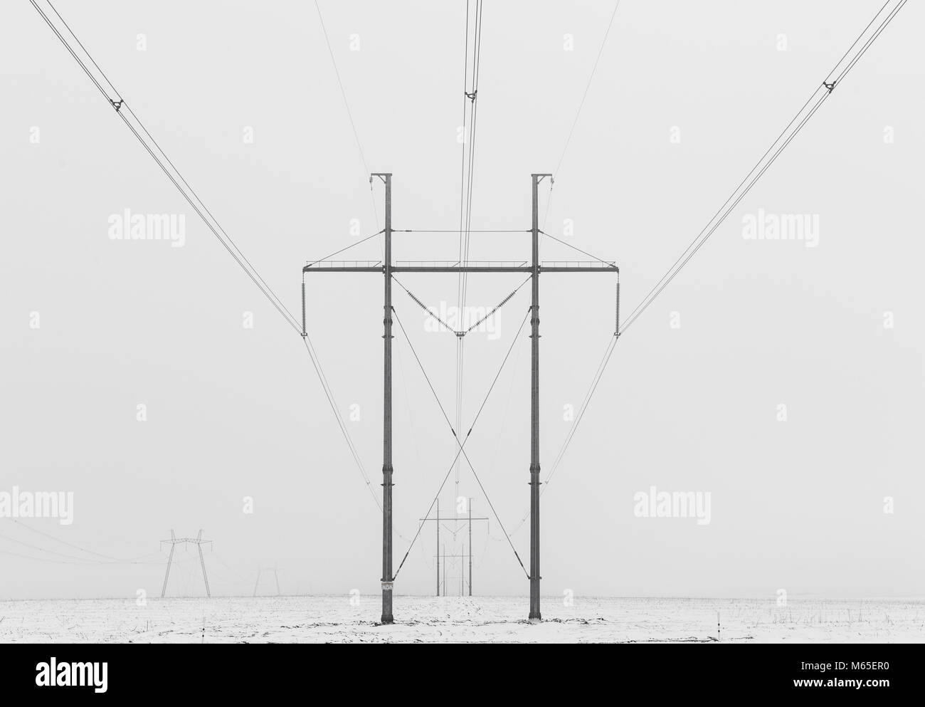 Hi-voltage electric power lines in a wintry foggy landscape, black and white photo. Stock Photo