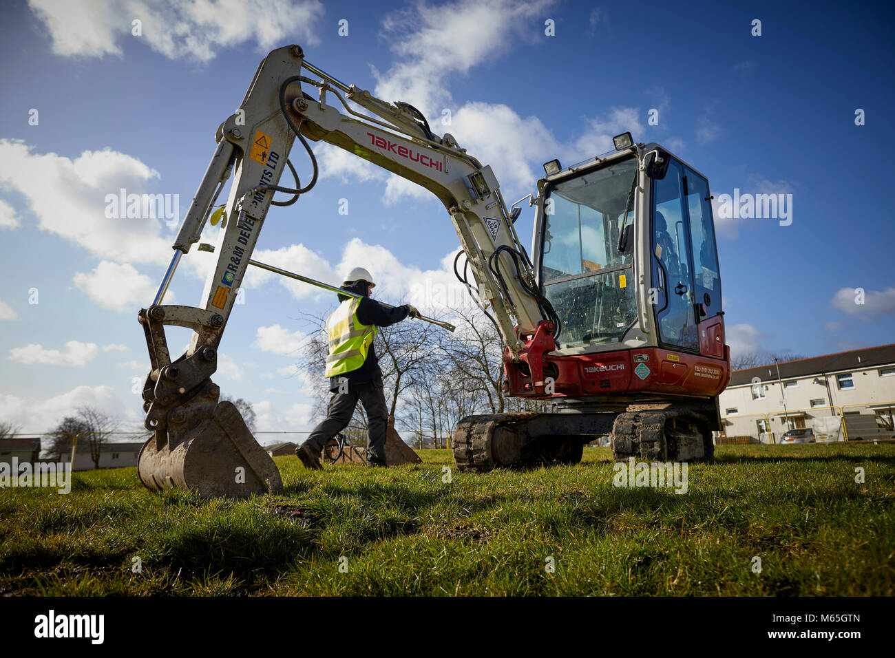 Workman on a building site next to a mini digger Stock Photo