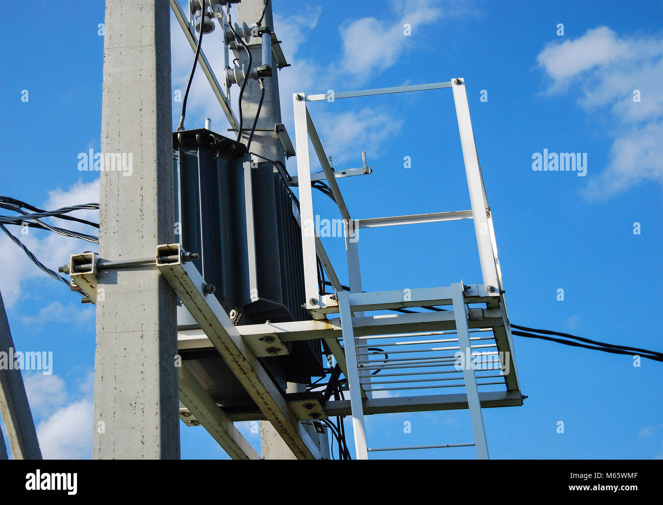 An electrical distribution transformer with cooling fins is located on the pole. Against the blue sky. Side view Stock Photo